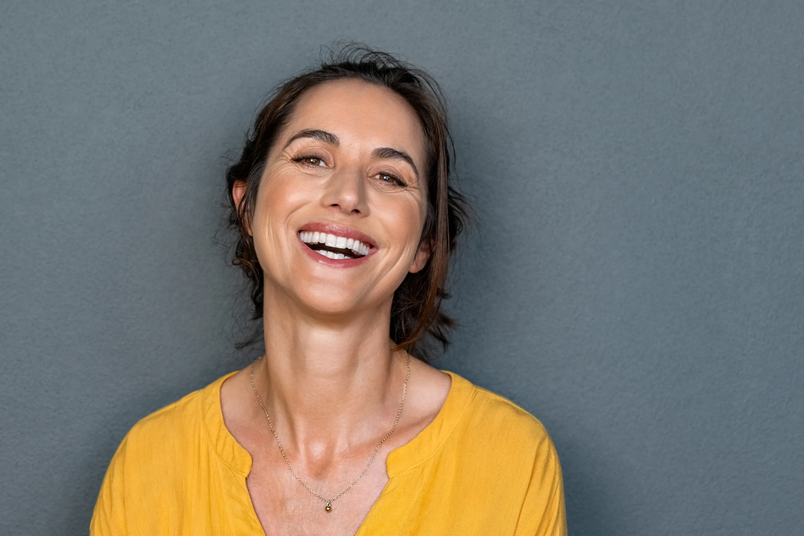 Smiling woman with smooth skin wearing a yellow top.