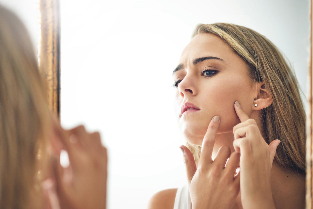 model trying to pop a pimple in the mirror