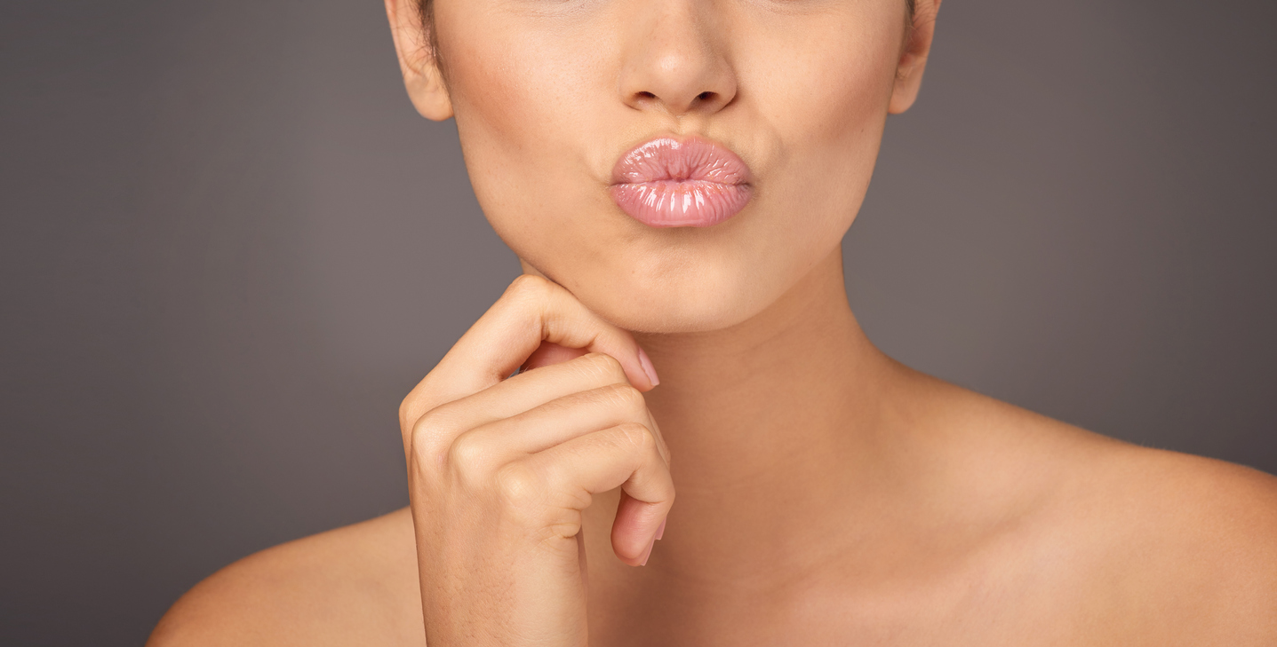Closeup studio shot of a woman with gorgeous glossy lips against a gray background