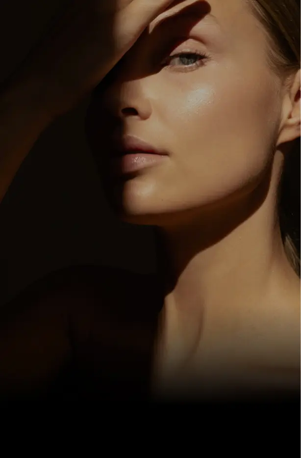 Elegant woman with radiant skin, partially shaded face highlighting smooth complexion.