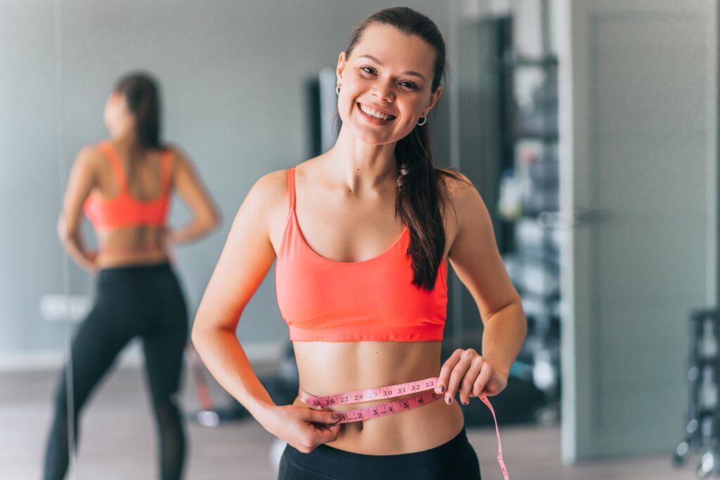 Woman measuring waist with tape in gym
