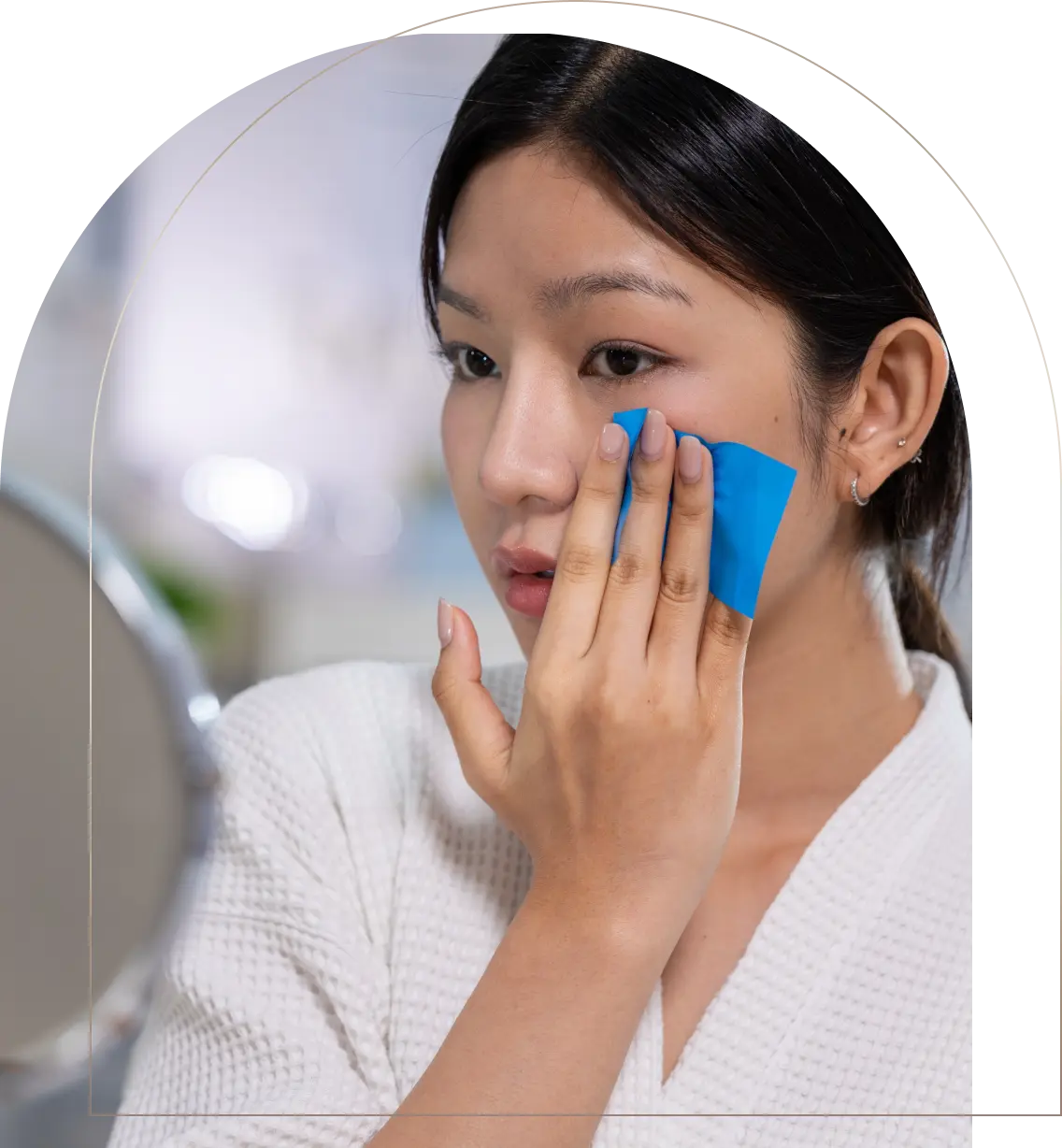 Young woman applying blue face patch under eye in bathroom mirror Woman applying blue under-eye patch