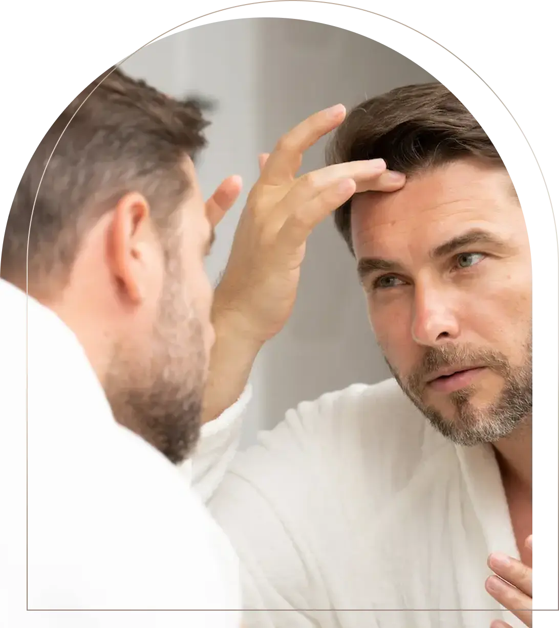 Man in white robe examining hairline in bathroom mirror Man checking hairline in bathroom mirror