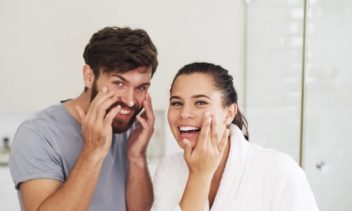 Couple applying facial moisturizer smiling