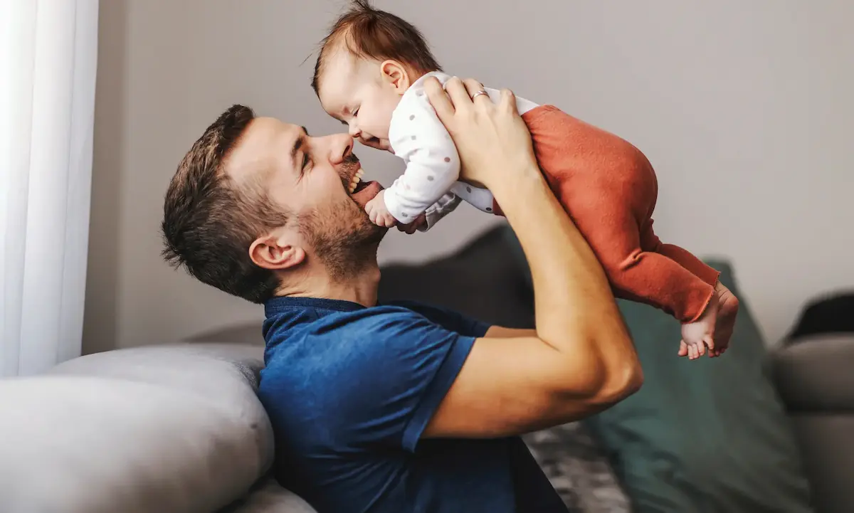 Father lifting smiling baby on couch