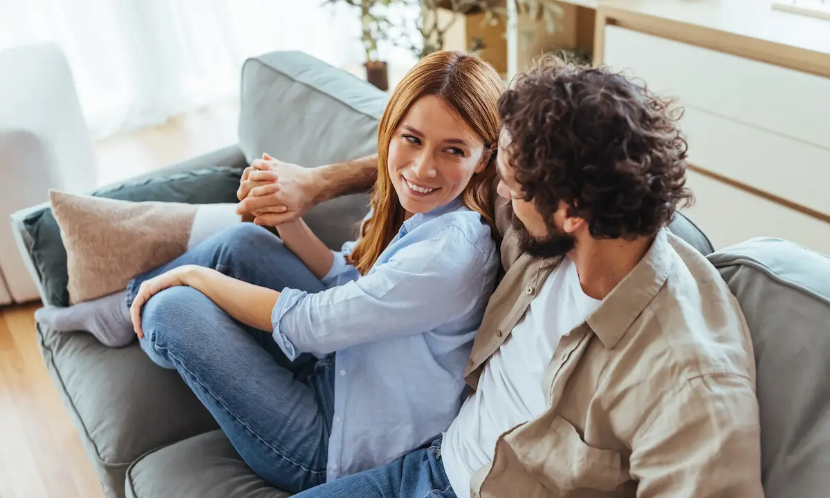 Couple holding hands sitting on sofa smiling